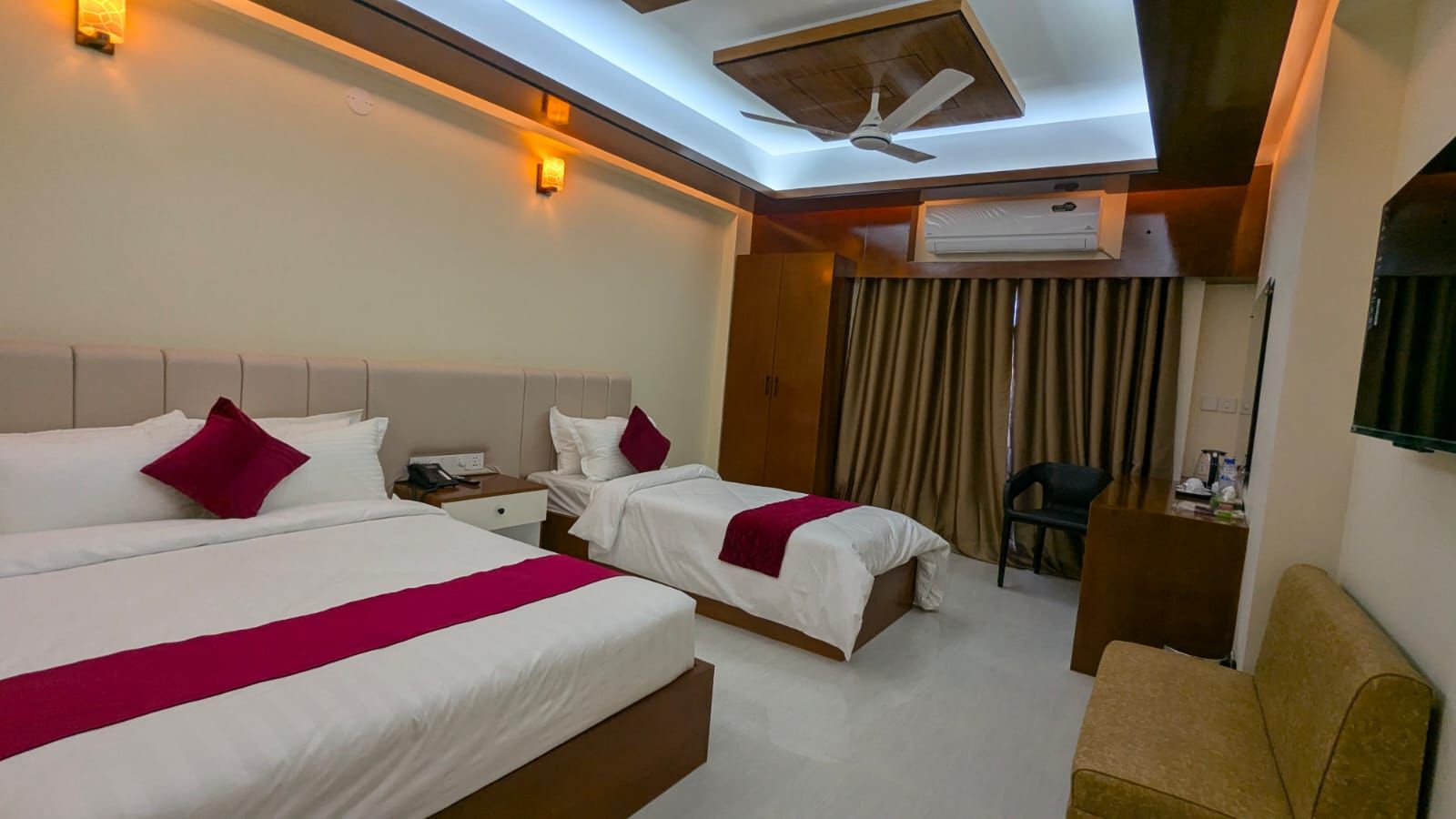 A hotel room with two beds, a ceiling fan, an air conditioning unit, a desk, and a chair.