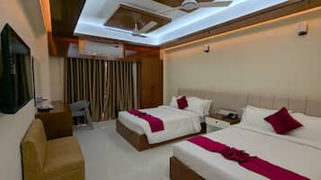 A hotel room with two beds, a ceiling fan, an air conditioning unit, a desk with a chair, and a television.