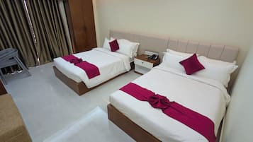A hotel room with two beds, each with white bedding and a red accent pillow. There is a nightstand with a phone and a remote control.