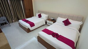 Une chambre d’hôtel avec deux lits, chacun agrémenté de draps blancs et d’un coussin décoratif rouge. On y trouve une table de chevet avec un téléphone et une télécommande.