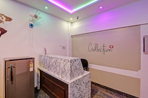 A reception desk with a marble top, a small fan, and a wall with the word 'Collection' written on it.