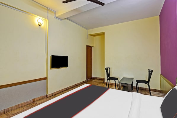 A hotel room with a bed, a flat-screen TV, a small table, two chairs, and a door.