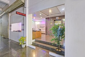 A reception area with a reception desk, a glass entrance, and a potted plant.