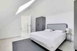 A modern bedroom with a skylight, a bed with white bedding, a grey wardrobe, and a bedside table with a lamp. - Elegant Appt - 3bdr/8p - Near Paris & La Defense (Suresnes)