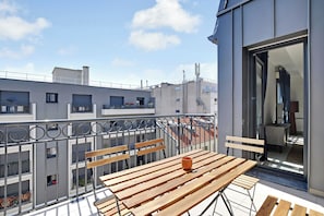 A balcony with wooden tables and chairs, a view of neighboring buildings, and a clear sky. - Elegant Appt - 3bdr/8p - Near Paris & La Defense (Suresnes)