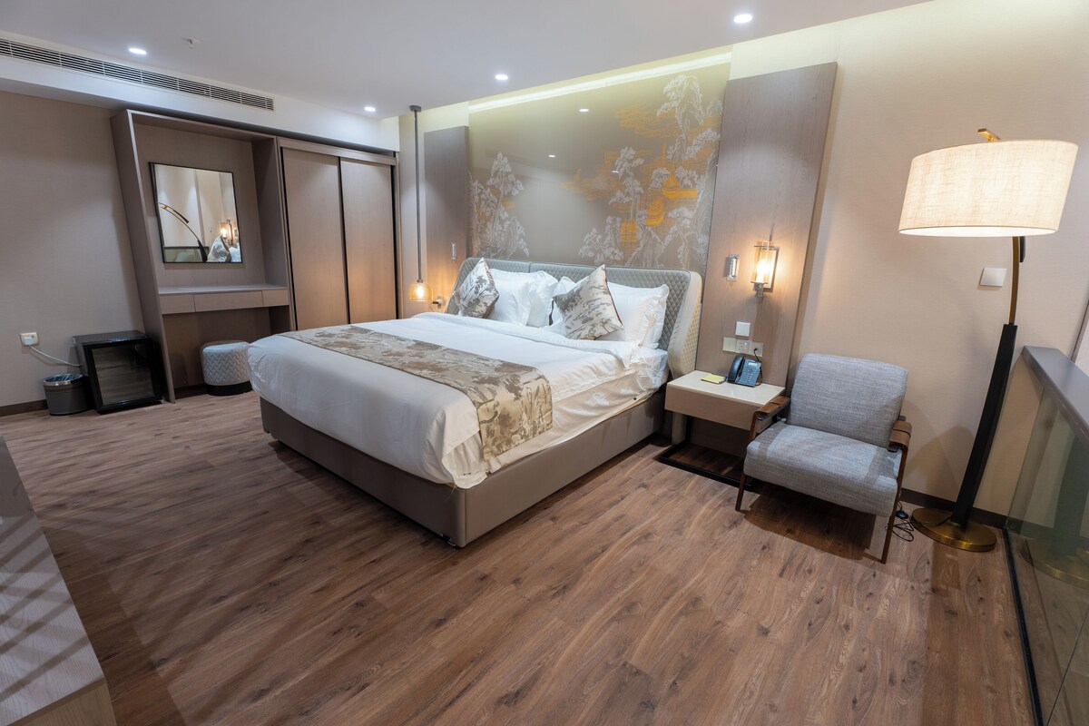 Une chambre à coucher moderne avec un grand lit, des tables de chevet, une chaise, un miroir et une lampe fixée au mur.
