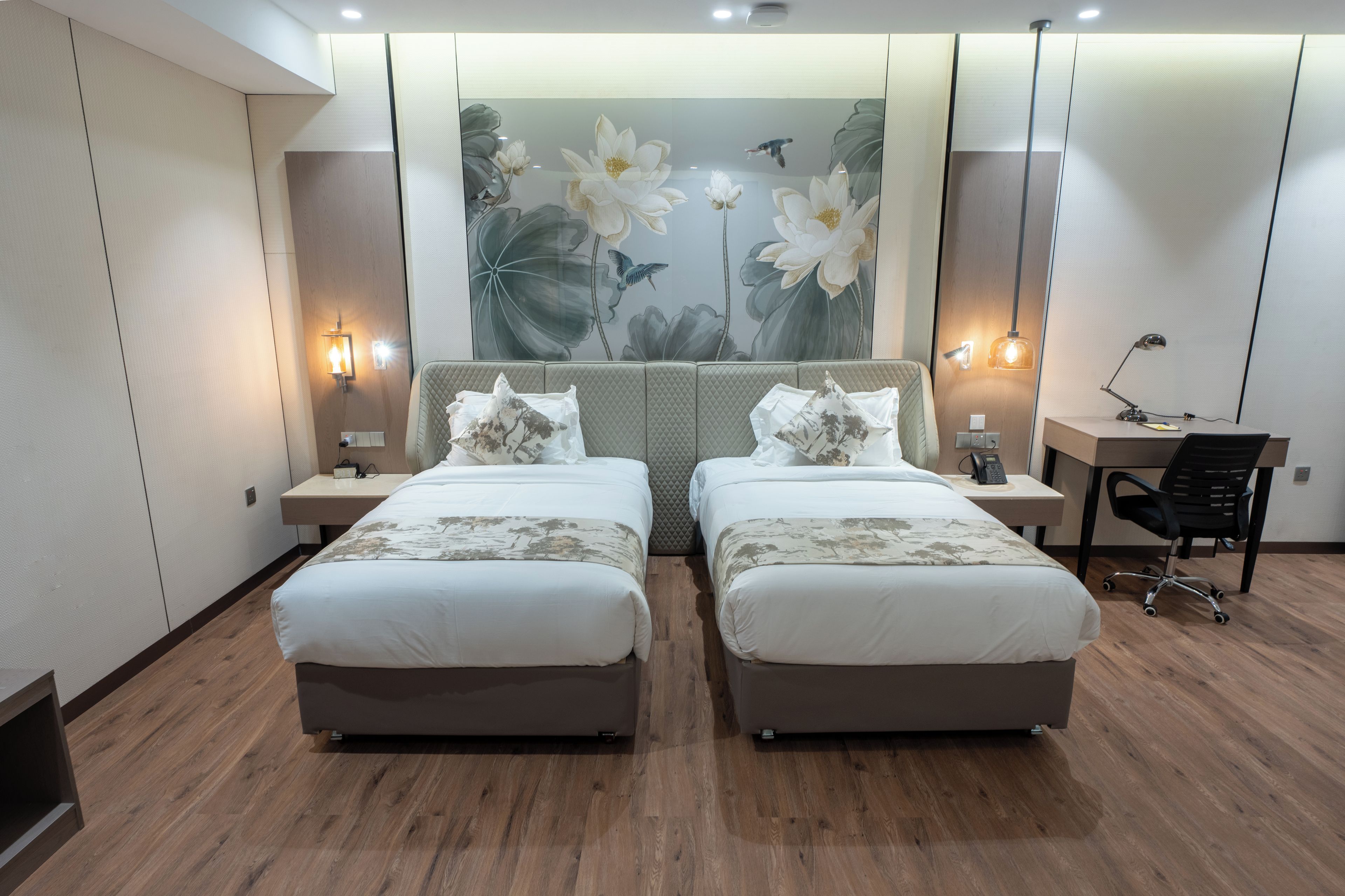 A hotel room with two beds, a large floral mural on the wall, a desk with a chair, and a phone.