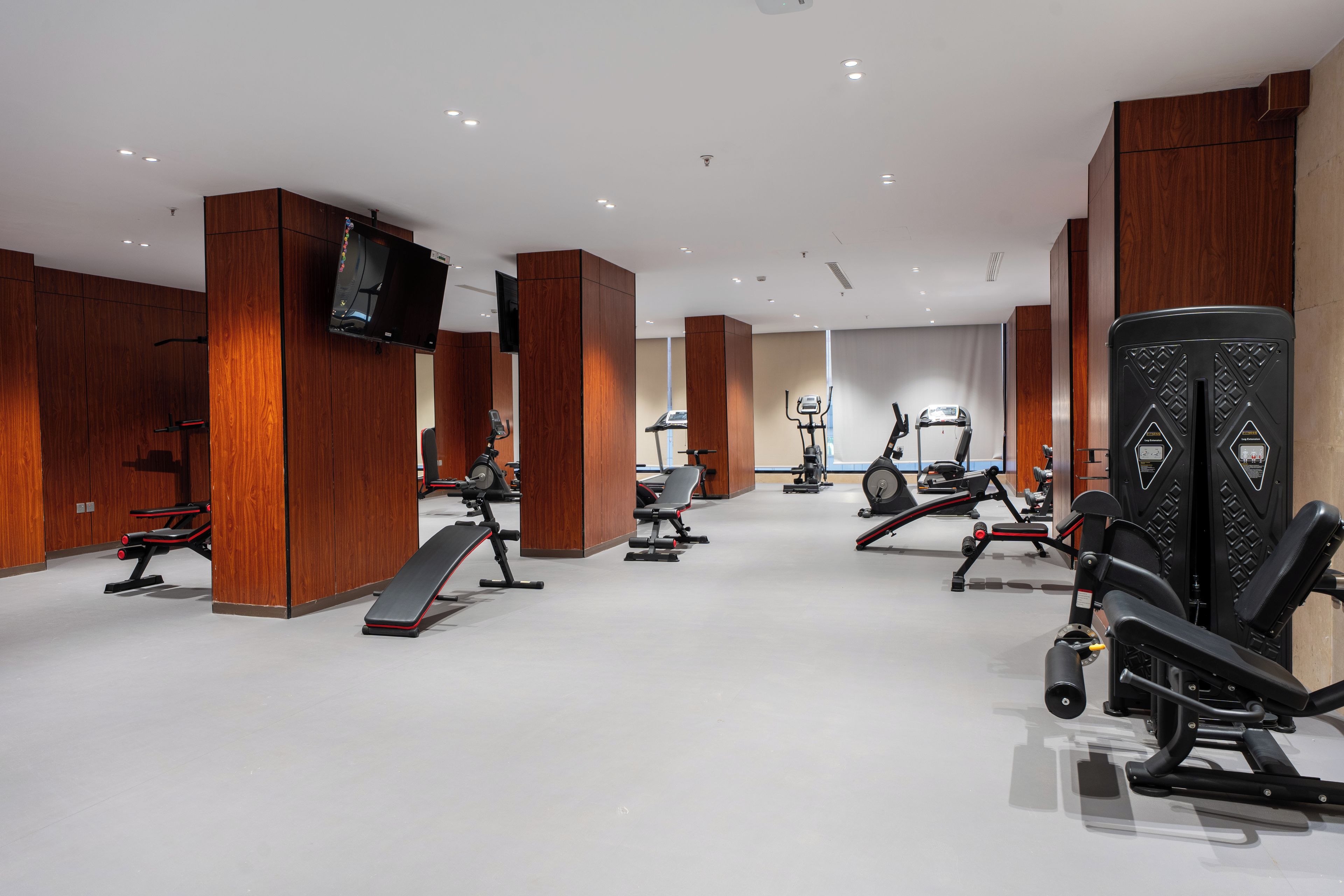Ein Fitnessraum mit unterschiedlichen Trainingsgeräten, Holzvertäfelung und einem an der Wand befestigten Flachbildfernseher.
