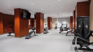 Ein Fitnessraum mit unterschiedlichen Trainingsgeräten, Holzvertäfelung und einem an der Wand befestigten Flachbildfernseher.