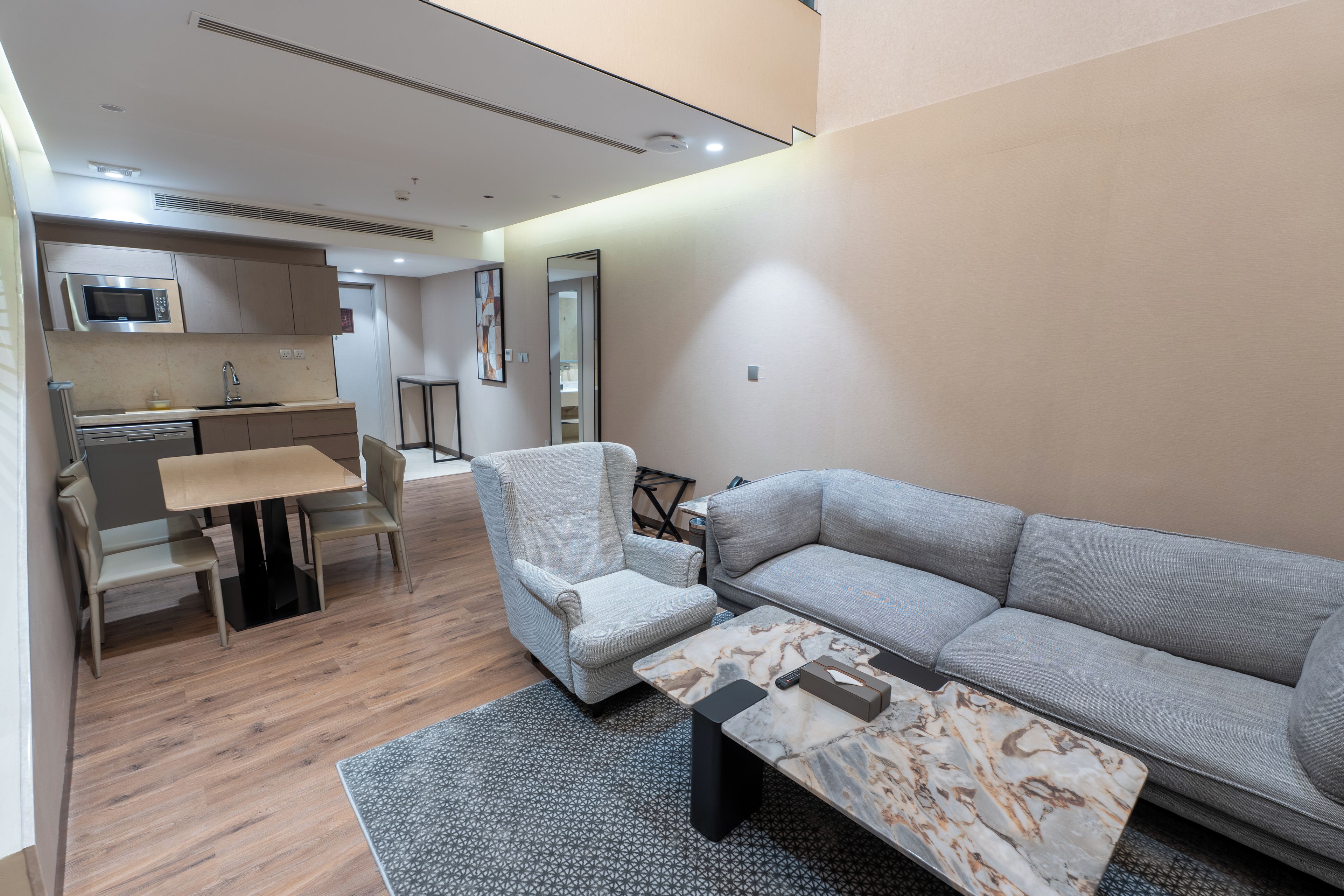 A modern living room with a grey sofa, a coffee table with a marble pattern, and a dining area with a kitchen in the background.