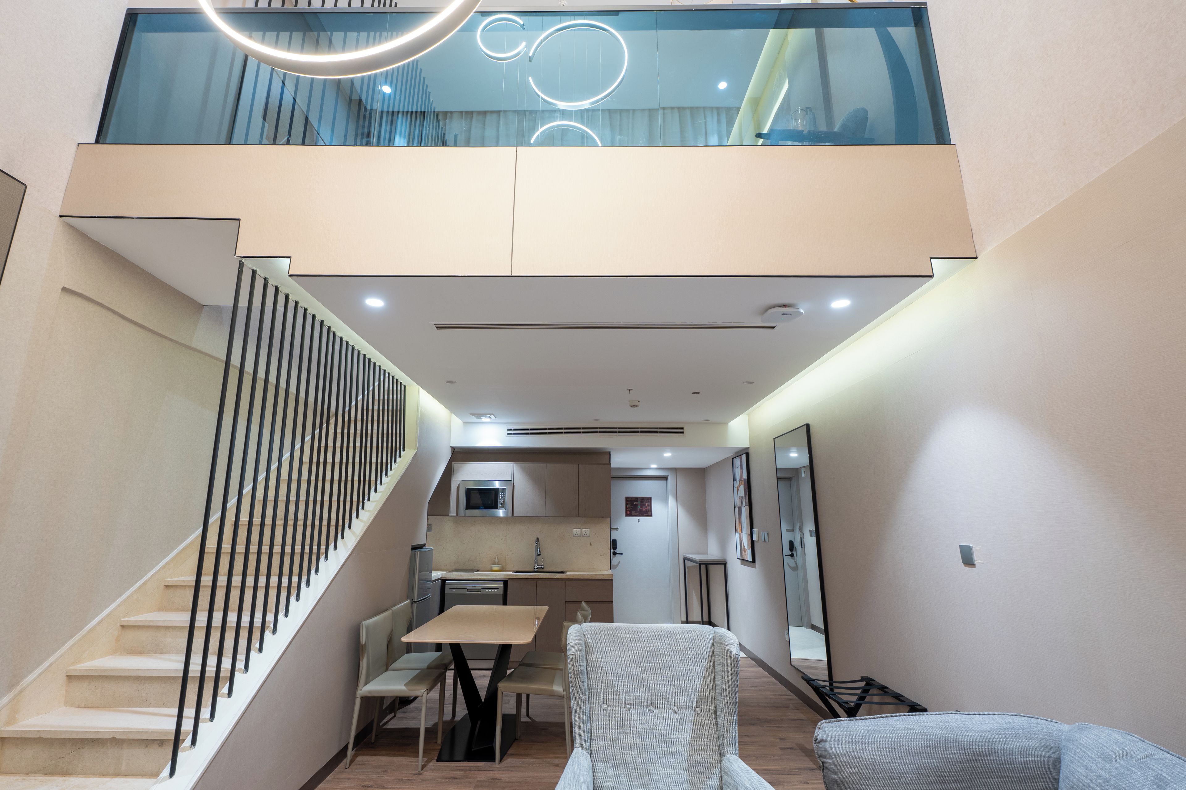 Ein modernes Interieur mit Treppe, Essbereich, Küche und einer oberen Ebene mit Glasgeländer.