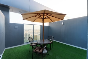 Un balcon avec une table et des chaises, un grand parasol et une vue sur la ville.