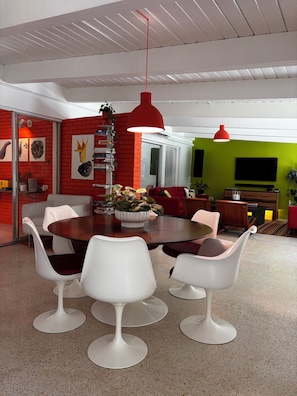 A modern dining area with a round table, white chairs, and red pendant lighting. - Mid-century designer home with pool and grill in plantation (Plantation)