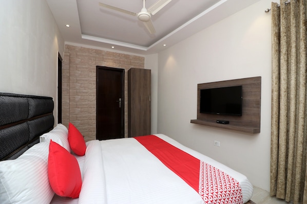 A modern bedroom with a bed, a television mounted on the wall, and a ceiling fan. - Hotel O Madhurapuri (Calicut)