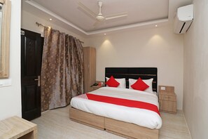 A bedroom with a bed, a nightstand, a wardrobe, a ceiling fan, and an air conditioning unit. - Hotel O Madhurapuri (Calicut)