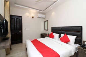 A hotel room with a bed, a desk, a TV, and an air conditioning unit. - Hotel O Madhurapuri (Calicut)