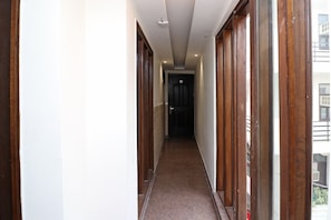 A narrow hallway with wooden doors and a carpeted floor, leading to a dark door at the end. - Hotel O Madhurapuri (Calicut)