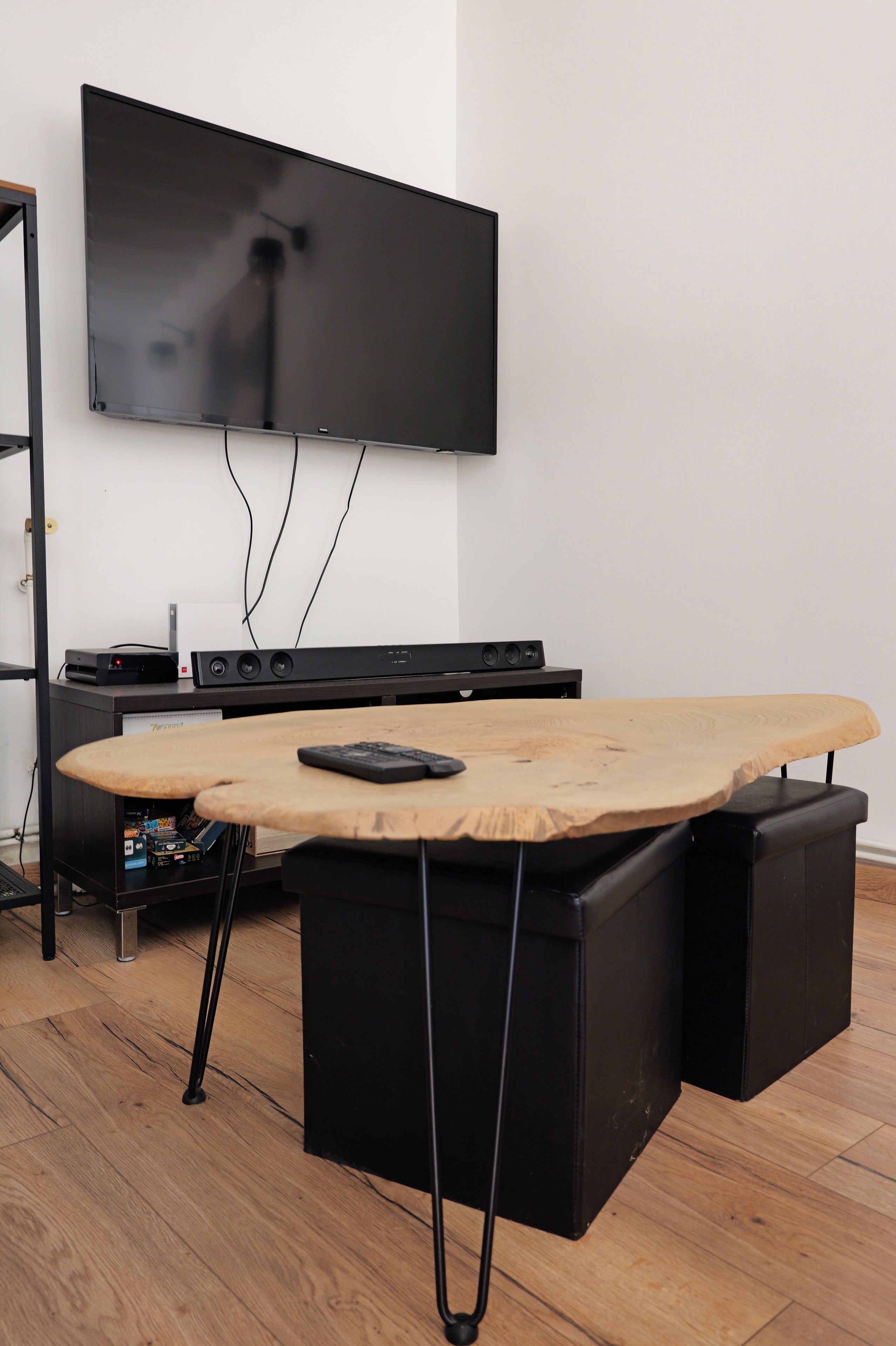 A room with a flat-screen TV mounted on the wall, a wooden table with a keyboard, and a black speaker.