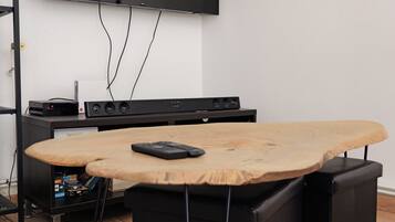 A room with a flat-screen TV mounted on the wall, a wooden table with a keyboard, and a black speaker.
