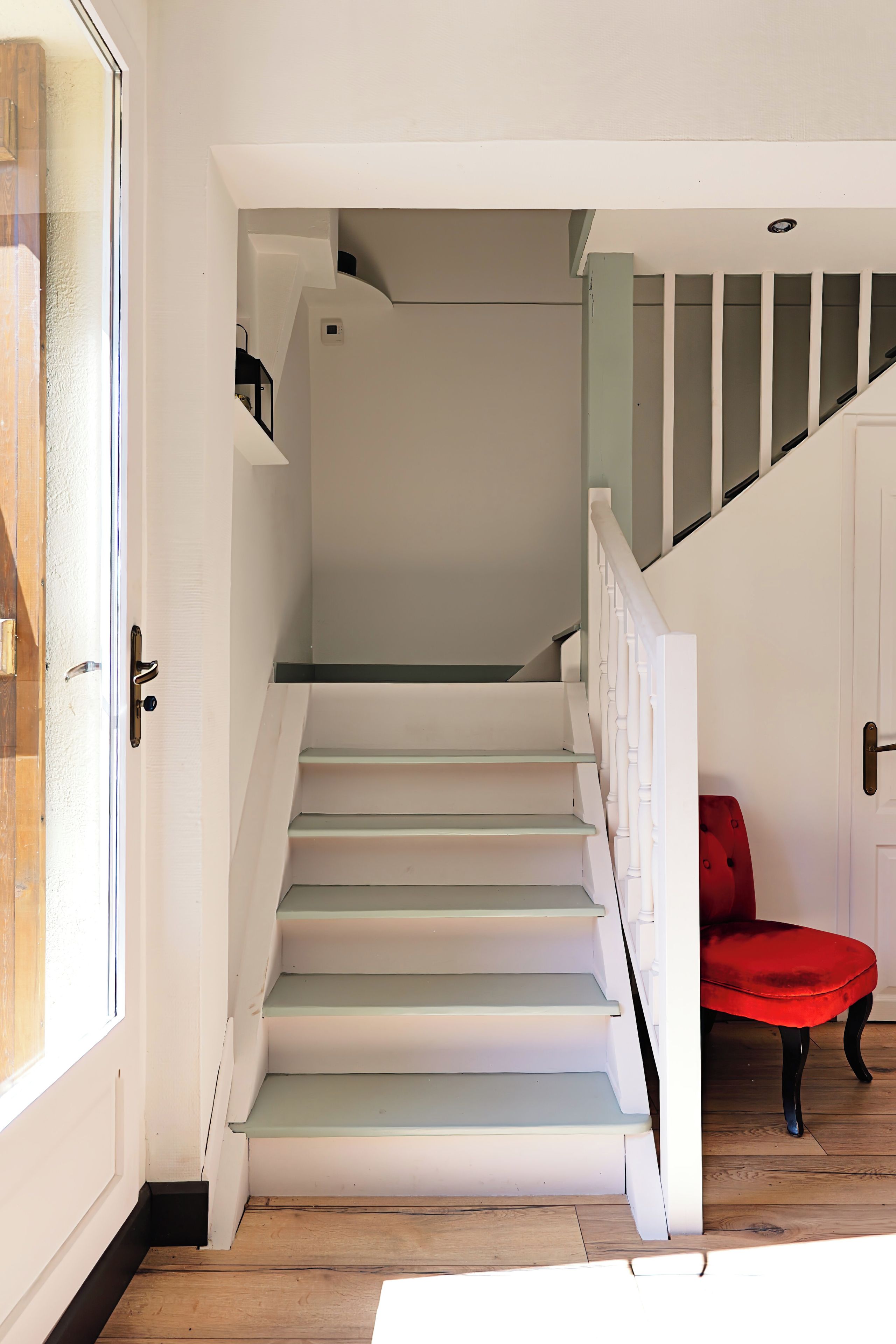 A staircase with white steps leading to a landing, a red chair, and a door with a white frame.