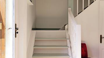 A staircase with white steps leading to a landing, a red chair, and a door with a white frame.