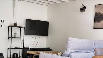A modern living room with a flat-screen TV mounted on the wall, a grey sofa, a wooden coffee table, and a ceiling light fixture.