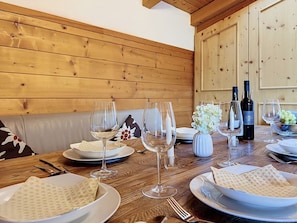 Una mesa de comedor de madera dispuesta con platos, vasos y cubiertos, junto con una botella de vino y un florero con flores.
