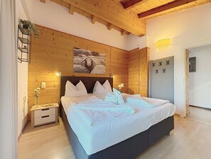 Ein Schlafzimmer mit Holzbalkendecke, einem Bett mit weißer Bettwäsche, einem Nachttisch und einem an der Wand befestigten Regal mit Pflanzen.