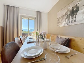 A dining area with a table set for two, a vase with flowers, and a painting of cows on the wall. - Nice apartment for 8 people with WIFI, TV, patio and pets allowed (Zell Am See)