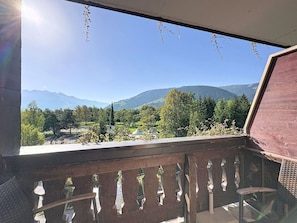Ein Balkon mit Blick auf eine gebirgige Landschaft, einem Holzgeländer und einem wolkenlosen Himmel.