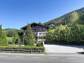 Ein mehrstöckiges Hotel mit einem Balkon im zweiten Stock, umgeben von üppiger Vegetation und einer Bergkulisse.