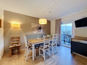 Ein stilvoller Essbereich mit einem Holztisch, weißen Stühlen, einem Gemälde an der Wand und Blick durch das Fenster.