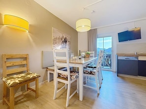 Uma área de refeições com mesa e cadeiras, um quadro na parede e vista pela janela.