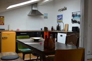 A compact kitchen with a dining table, chairs, a small refrigerator, and various kitchen appliances. - Anna Thomsen Foundation Apartment with Rooftop Terrace (Flensburg)