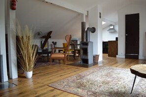 A living room with a fireplace, wooden flooring, a dining area with chairs, and a large rug. - Anna Thomsen Foundation Apartment with Rooftop Terrace (Flensburg)
