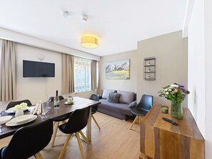 Ein modernes Wohnzimmer mit Essbereich, einem flachbildfernseher an der Wand, einer Couch und einem Couchtisch.