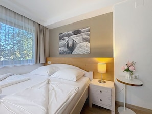 Quarto de hotel com cama, mesa de cabeceira, abajur, vaso com flores e um quadro na parede.