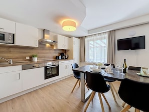 Eine moderne Küche mit weißen Schränken, einem eingebauten Ofen und einem Essbereich mit Holztisch und Stühlen.