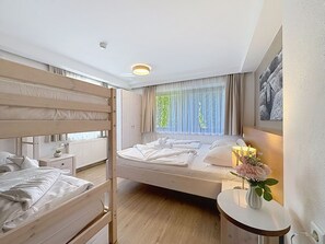 A hotel room with a bunk bed, a single bed, a bedside table with a vase of flowers, a window with curtains, and a radiator. - Nice apartment for 6 people with WIFI, TV, patio and pets allowed (Zell Am See)
