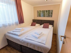 Ein Doppelbett mit weißer Bettwäsche und zwei Kissen, ein Holzboden, ein Fenster mit transparenten Vorhängen und ein Bild an der Wand.