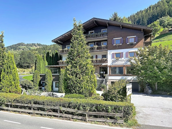 Ein mehrgeschossiges Gebäude mit Balkonen, einem Schild für 'Edelweiss Apartments' und einer umliegenden Landschaft mit Bäumen und Hügeln.
