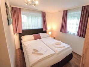 A hotel room with a bed, two bedside lamps, a window with curtains, and a wall-mounted light fixture. - Cosy apartment for 4 people with WIFI, TV, patio and pets allowed (Zell Am See)