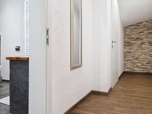 Ein Korridor mit Holzboden, weißen Wänden und einer Steinwand mit strukturierter Oberfläche.
