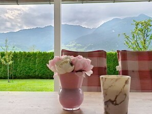 Ein Tisch mit Blumen in einer Vase und einem Glas, vor einer Berglandschaft.
