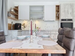 Eine moderne Küche mit eingebauten Geräten, eine Essecke mit einem Holztisch für zwei Personen und eine Sitzecke mit einer Couch.