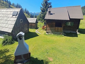 Eine rustikale Holzhütte mit geneigtem Dach, umgeben von einer gepflegten Rasenfläche und einem Blick auf die Berge.