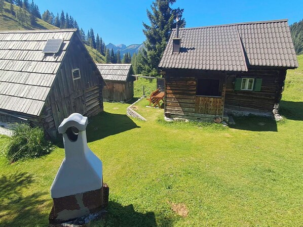 Una cabaña de madera rústica con techo inclinado, rodeada de césped cuidado y con montañas al fondo.