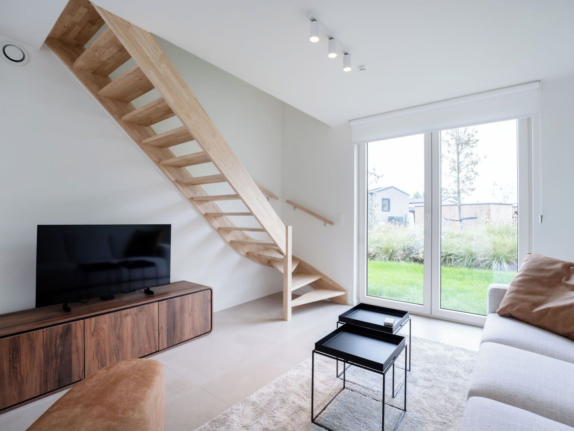 Een moderne woonkamer met een houten trap, een flatscreen televisie, een bank en een salontafel.