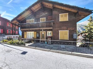 Un bâtiment en bois à deux étages, doté d’un balcon, d’une enseigne indiquant « Chalet Eliane » et offrant une vue sur les montagnes en arrière-plan.