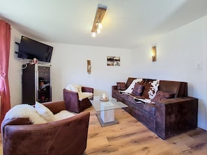 Ein Wohnzimmer mit einer Couch, einem Sessel, einem Flachbildfernseher und einem Couchtisch.
